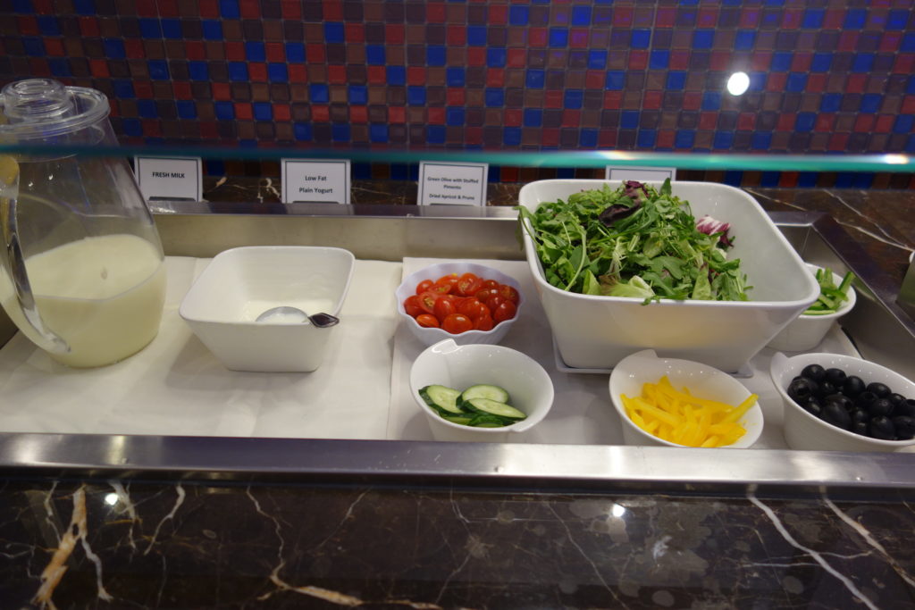 a salad bar with different bowls of vegetables and a glass of milk