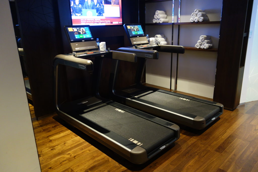 a treadmills with laptops and a tv on the wall